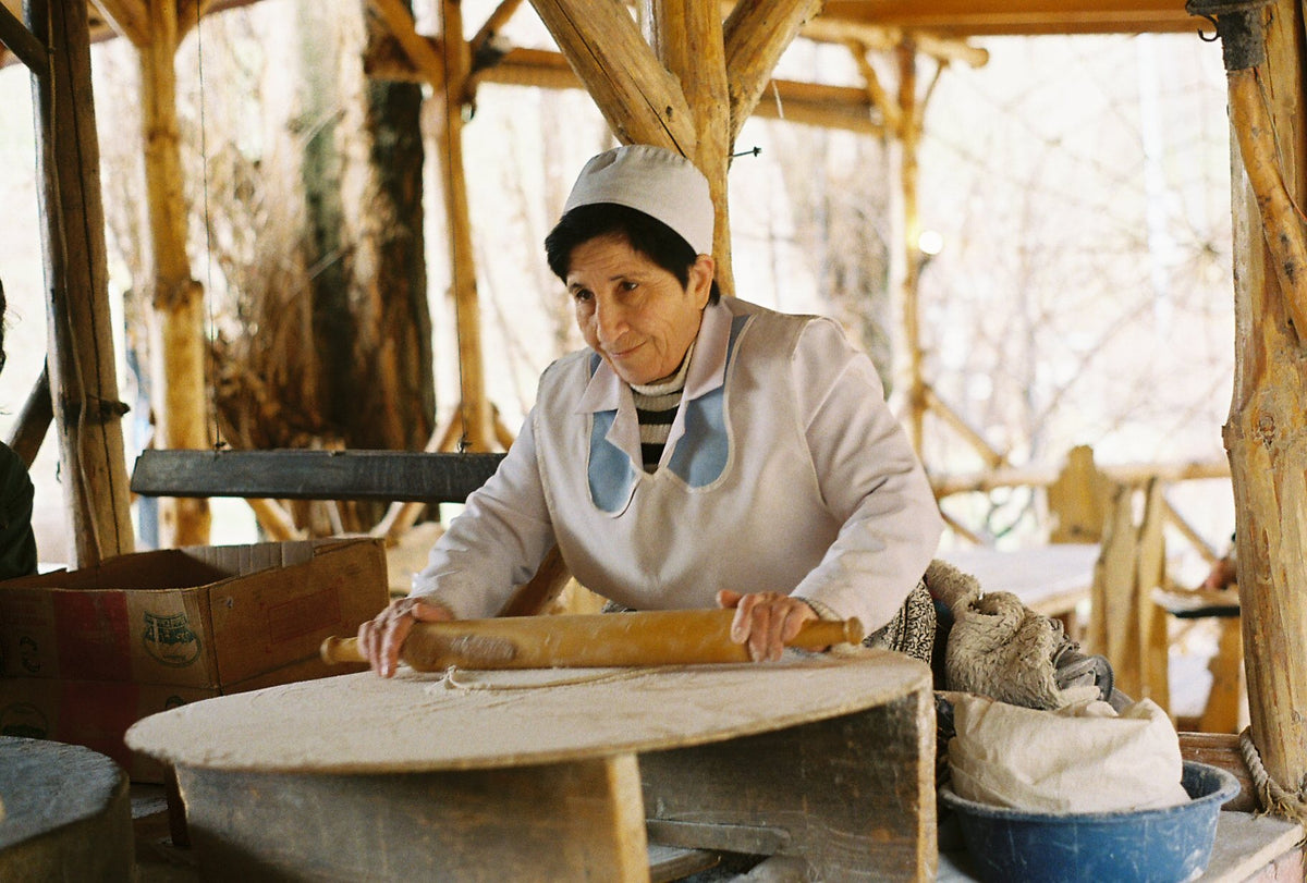 A woman rolls lavash dough by hand on a wooden board