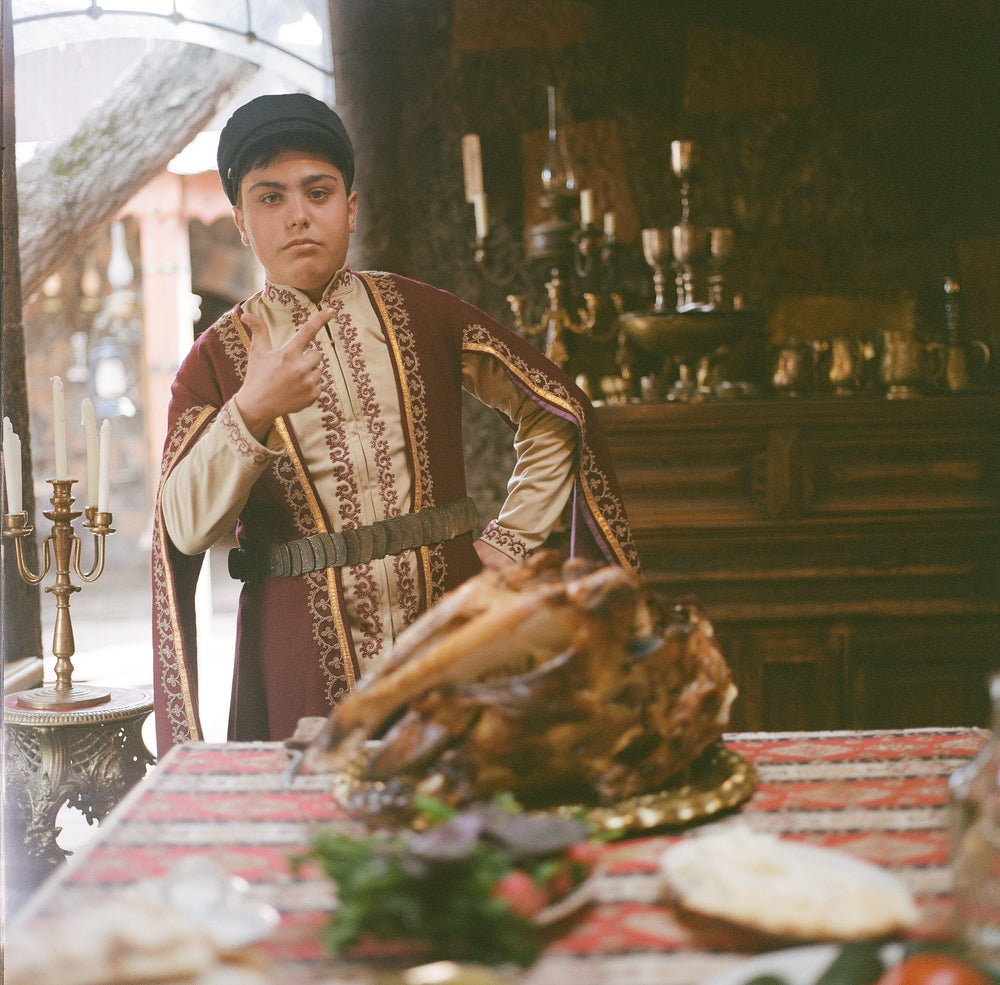 A young man in traditional Armenian dress beside a feast table
