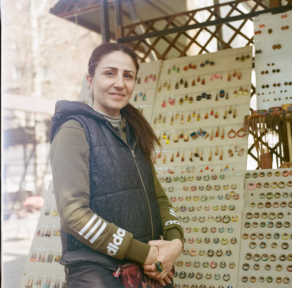 A market vendor stands before a display of handmade earrings