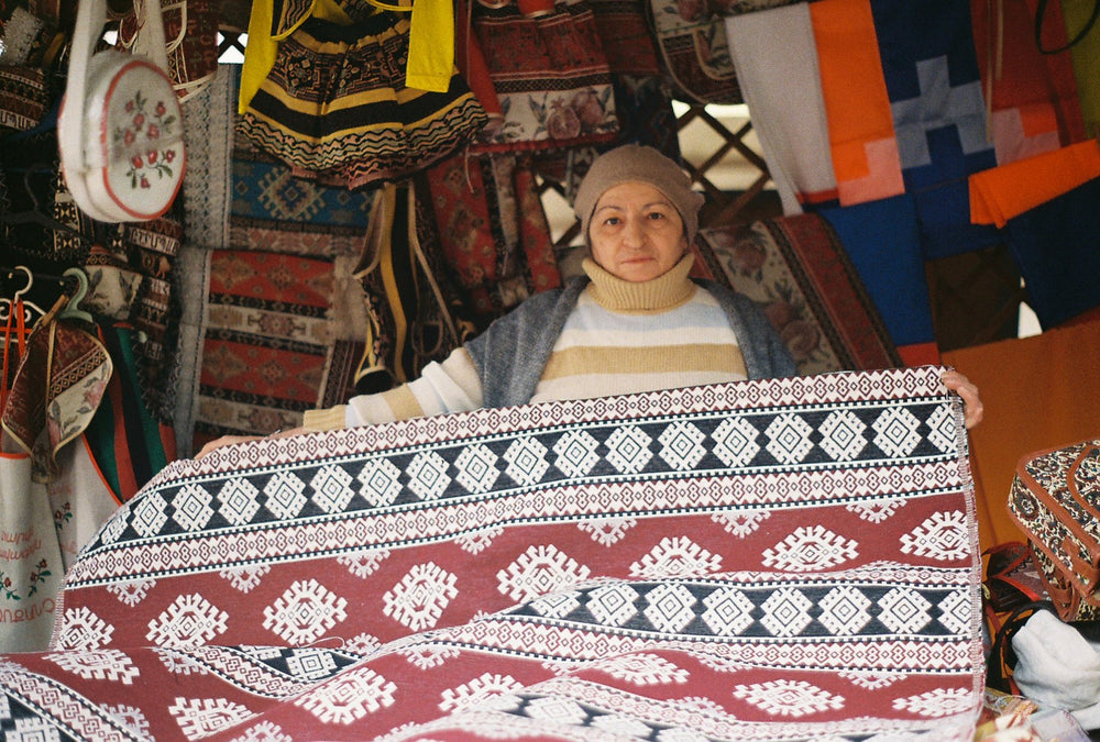 A textile seller surrounded by woven carpets and embroidery